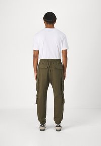 Olivgröna cargobyxor med elastisk midja, sidofickor och ribbade muddar. I kombination med en enkel vit t-shirt och svarta sneakers.