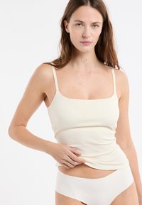 Débardeur côtelé beige clair avec fines bretelles et encolure carrée, assorti à une lingerie sans coutures. Tissu doux et extensible.
