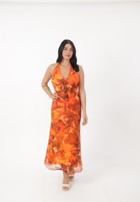 Oranje maxi-jurk met halternek, voorzien van een bloemenontwerp, een getailleerde taille en een vloeiende zoom. Het materiaal lijkt licht en doorschijnend.
