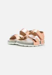 Roze gouden sandalen met dubbele kruisbanden, zilveren gesp, zacht grijze voetbed en witte gestructureerde rubberen zool.