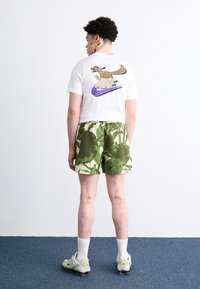 Hvid t-shirt med et cartoon-kangaroo grafik og lilla Nike-logo, parret med grønne og beige mønstrede shorts og grå sneakers.