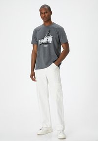 Camiseta de algodón gris con un gráfico de mano en blanco y negro que dice "Okay", combinada con pantalones cargo blancos y zapatillas blancas.