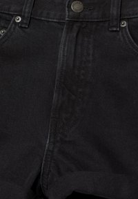 Blugi din denim negru, prim-plan care arată detalii precum nasturele din față, zona fermoarului, bucle pentru curea și nituri de la buzunare.