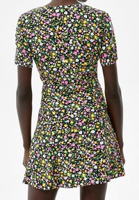 Sukienka z krótkim rękawem wykonana z czarnego materiału, z kolorowym kwiatowym wzorem w odcieniach różu, żółci i zieleni, z dopasowaną talią i rozkloszowanym dołem.