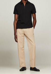 Svart kortärmad polo med dragkedja i kragen, tillsammans med beige lätta byxor och svarta loafers. Enkel och modern design.