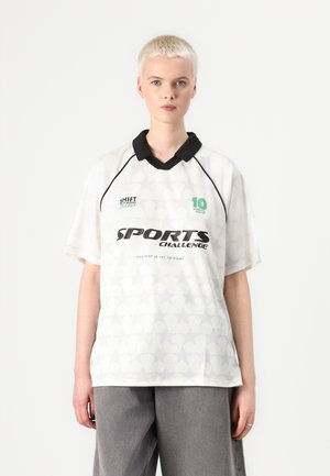 Valkoinen urheilupaita mustalla kauluksella, jossa on tähden kuvio ja etupuolen teksti "SPORTS CHALLENGE." Vihreät yksityiskohdat kaula-aukossa ja sivuilla.