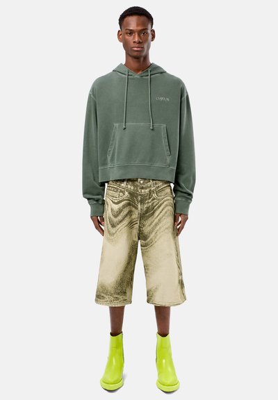 Olijfgroene cropped hoodie met een voorzak, gecombineerd met metaal gouden knielange shorts en glanzende limoen groene enkellaarzen.