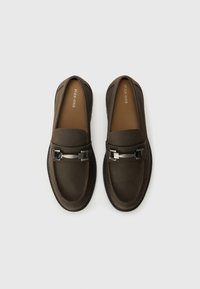 Mocasines marrones sin cordones con una textura suave, herrajes de acento metálico y un diseño de punta redonda con una suela contrastante.