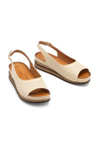 Beżowe sandały na obcasie z otwartym noskiem, perforowanym wykończeniem, wyściółką z poduszką i korkowym obcasem.