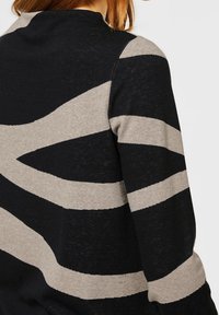 Sweter dziany z geometrycznym wzorem, w którym naprzemiennie występują czarne i jasnobeżowe paski, charakteryzujący się miękką teksturą i smukłą sylwetką.