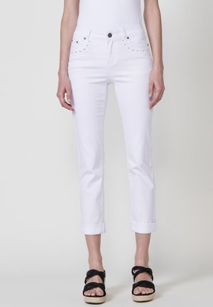 Jean en denim blanc avec une coupe slim, munis de poignets roulés, de poches avant avec des embellissements et d'une fermeture à bouton classique.