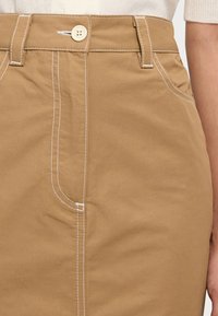 Kohanest valmistatud seelik, millel on valge õmblus, esine nööp sulgemine ja kitsas sobivus küljetaskudega.