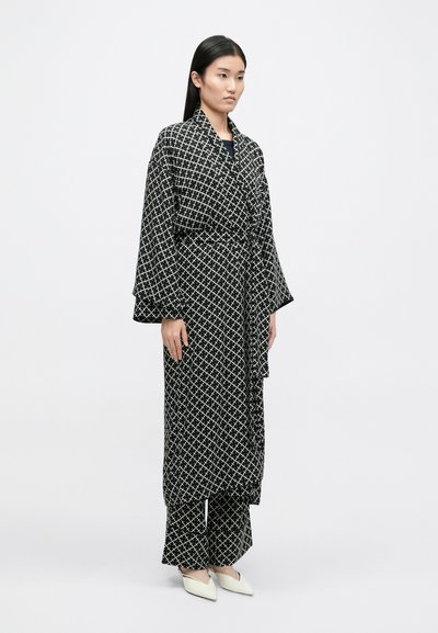 Μαύρο και λευκό ριγέ ρόμπα με φαρδιά μανίκια, δεμένη στη μέση, και ταιριαστά παντελόνια με φαρδιά πόδια; λεία ύφασμα με γεωμετρικό σχέδιο.