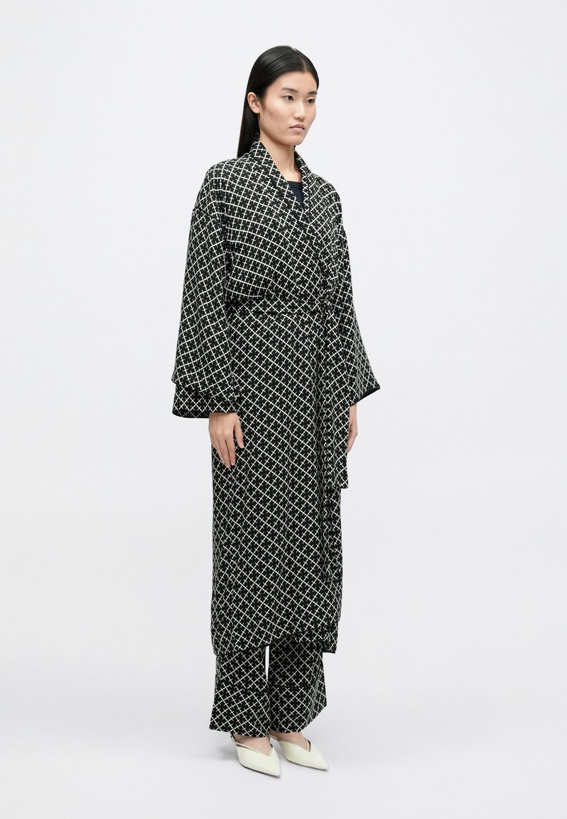 Schwarz-weiß gemusterter Morgenmantel mit weiten Ärmeln, in der Taille gebunden, und passenden weiten Hosen; glattes Material mit geometrischem Design.
