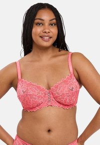 Roze kant bralette met bloemmotieven, geschulpte randen en een decoratieve voorkant met vetersluiting. Gladde, verstelbare bandjes.