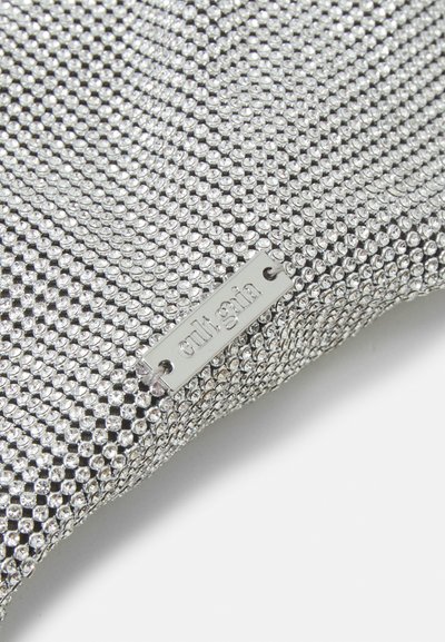 Material din plasă argintie cu o suprafață texturată acoperită de mici nituri strălucitoare. Include o etichetă metalică cu inscripția "cult gin."