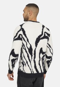 Pull pour homme en crème avec un motif zèbre noir texturé, doté de manches longues et d'un ourlet côtelé. Tissu doux et duveteux.
