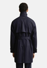 Granatowy płaszcz trench z paskiem w talii, detalami na guzikach i tylnym klapą. Posiada wysoki kołnierz oraz długie rękawy z regulowanymi mankietami.
