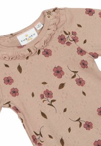 Bézs hosszú ujjú ruhadarab rózsaszín és barna virágmintával. Ráncolt nyakkivágással és patentgombos záródással. Puha tapintású.