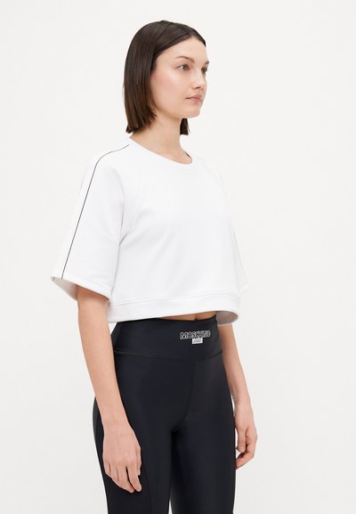 Vit kortärmad sporttopp med texturerad tyg och svarta accenter, tillsammans med högmidjade svarta leggings med en logotyp på midjebandet.