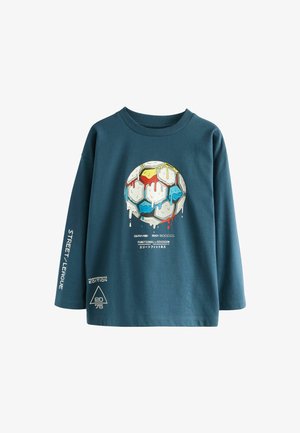 Hosszú ujjú teal színű pamut póló, amelyen egy színes grafikájú, csöpögő focilabda és szöveges díszítések találhatók az ujjakon és a szegélyen.