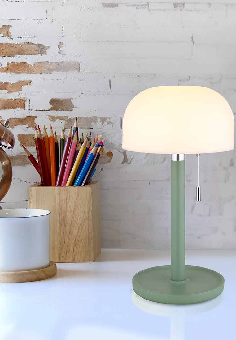 Lampada da tavolo con una sfera di vetro opalino tondo, base e stelo verdi, e una catena di sospensione. Sullo sfondo, matite colorate e una tazza bianca.
