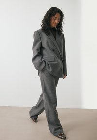 Halli villane ülikond, mis sisaldab kahekordse pingutusega ülikonda ja laiad püksid, millel on tekstuuriga viimistlus ja siledad tumedad kingad.