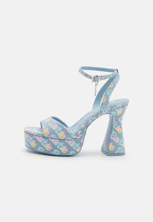 Sandali platform blu cielo con tacco spesso, caratterizzati da un motivo ripetuto "Barbie" in rosa e giallo. Cinturino alla caviglia con dettaglio metallico.
