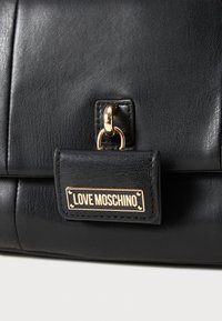 Black leather bag detail with gold clasp and "LOVE MOSCHINO" engraved gold nameplate on front flap.