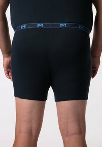 Boxer shorts in cotone neri con vita elastica blu che presenta un logo. Tessuto liscio con design aderente, che copre fino a metà coscia.