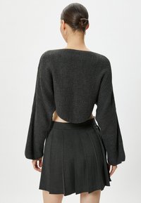 Maglione a collo alto grigio scuro a maglia corta con maniche ampie e schiena scoperta, abbinato a una gonna plissettata grigio scuro con vita alta.
