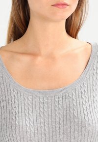 Pullover grigio chiaro in maglia che presenta un design a costine con un ampio scollo. La trama mostra sottili motivi a trecce. Tessuto morbido ed elastico.
