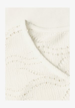 Tissu blanc texturé avec un motif diagonal de petits trous et un bord plié sur un fond blanc uni.