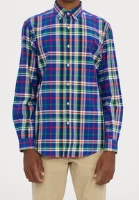 En knäppt skjorta med ett rutmönster i blått, grönt, rött och vitt. Har krage, långa ärmar och vita knappar.