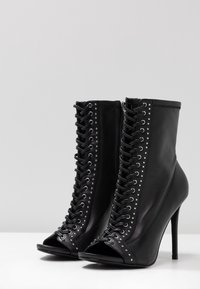 Stivaletti neri con tacco alto e punta aperta, caratterizzati da una chiusura lace-up e borchie decorative argentate lungo i lati. Realizzati in pelle.