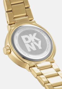 Goldfarbene Edelstahl-Armbanduhr mit rundem Gehäuse, gebürstetem silbernen Rückenteil, gekennzeichnet mit "DKNY", und einem polierten flachen Armbanddesign.