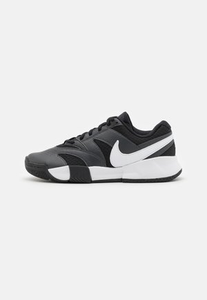 Zapatilla Nike negra y gris con logo swoosh blanco, cordones negros y suela segmentada blanca y negra, vista lateral sobre fondo neutro.