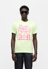 Ανοιχτό πράσινο κοντομάνικο μπλουζάκι με μεγάλο ροζ γραφικό σχέδιο και κείμενο, καθώς και ένα χαμογελαστό σύννεφο. Φορεμένο με μαύρο αθλητικό παντελόνι.