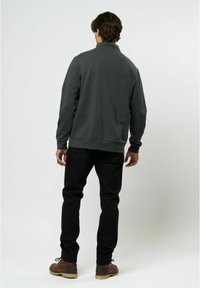 Sudadera gris oscuro con un cuello alto, puños y dobladillo de canalé; combinada con jeans negros y zapatos marrones, vista desde atrás.