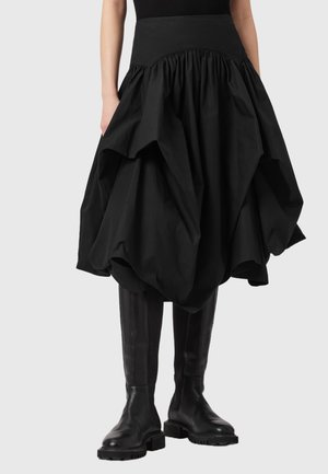 Sort, oversized nederdel med samlet tekstur og voluminøs form, med en høj talje og glat stof. Kombineret med knæhøje sorte støvler.