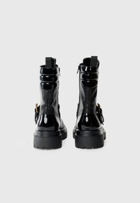 Botines de charol negro con suela gruesa, cremalleras laterales y elementos decorativos. Presentan paneles texturizados y tiradores para mayor comodidad.