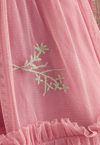 Tissu en maille rose avec broderie florale vert clair et détail de volants froncés le long du bord inférieur.