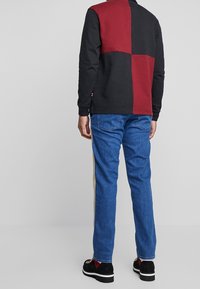 Svart och vinröd färgblockerad sweatshirt med långa ärmar, tillsammans med blå denimjeans och svarta skor med röda accenter.