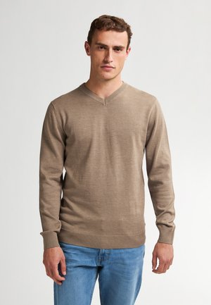 Beige V-Ausschnitt Pullover aus weichem Material, mit langen Ärmeln und gerippten Bündchen, kombiniert mit hellblauen Jeans.