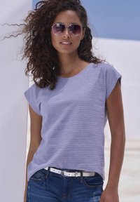 Lavender striped short-sleeve top with a round neckline, paired with blue jeans and a white belt. Model wears silver sunglasses.