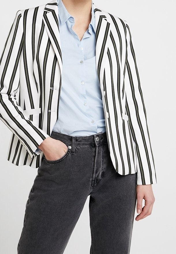 Pruhované sako v černé a bílé barvě, s na míru šitým střihem a úzkým střihem, nošené přes světle modrou košili a doplněné tmavými džínami z denimu.