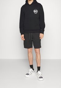 Black hoodie with a circular logo, paired with dark shorts, and white sneakers with black accents. Simple design and relaxed fit.