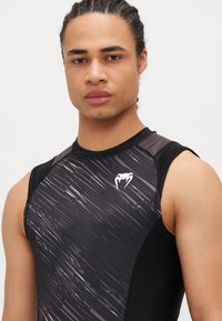 Must hüpik must sporditop graafilise disainiga, millel on triibud. Võrkkanga aktsendid ja väike valge logo rinnal.