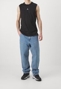 Svart ärmlös skjorta med vitt logotyp, ljusblå baggy jeans och svarta sneakers. Avslappnad passform med tydliga fickor och sömmar.