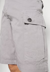 Pelēki kravas šorti izgatavoti no viegla auduma ar sānu kabatu, zīmola logotips izšūts un pogu detaļa netālu no jostasvietas.